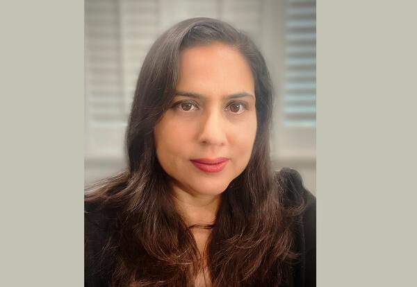 Dr. Patricia Sandoval with a composed expression, her long, dark hair framing her face. She wears a black outfit and subtle makeup with red lipstick, presenting a professional appearance. The background is neutral with soft lighting and blurred white wind