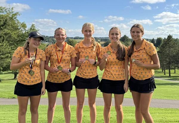 five girls in golf uniforms holding medals