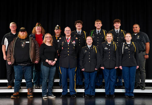 service members and student JROTC members pose onstage in a group