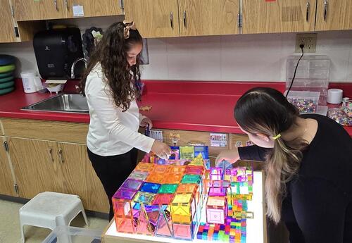 two girls play with a table full of plastic building blocks