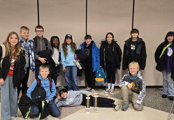 twelve elementary students pose in front of two trophys