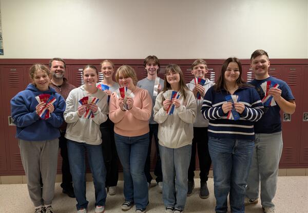 students and advisor stand in school hallway holding up award ribbons