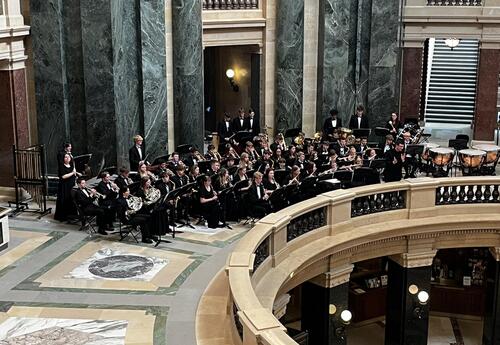 student musicians performing, seated on rotunda balcony with large marble columns behind them