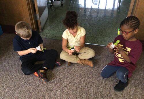 Students sitting together on classroom floor holding plants