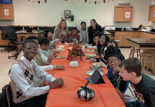 Students and staff smiling and gathering around a classroom table