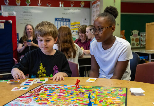 An older student helps a younger one play Candy Land