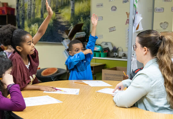 Second graders raise their hands in a small group