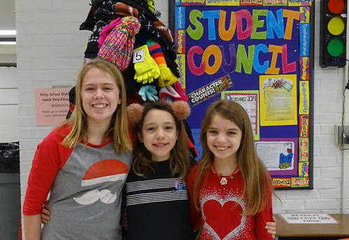 three smiling students standing in front of christmas tree