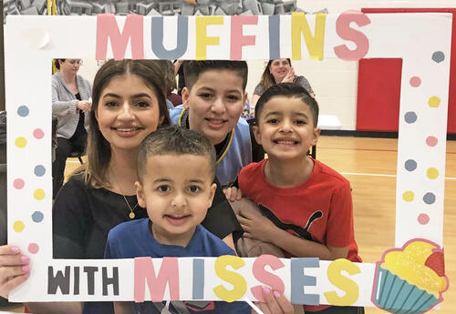Mother poses with three sons holding Muffins with Misses Sign