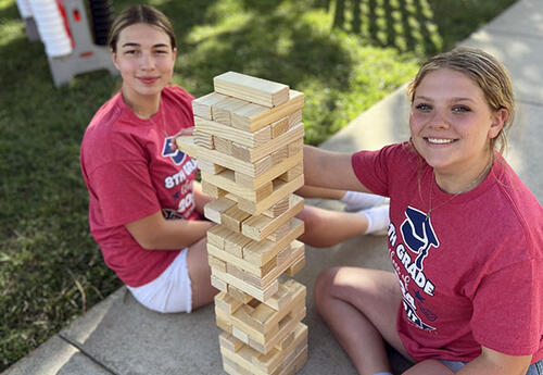 Students smile while playing a wooden stacking tower game outside