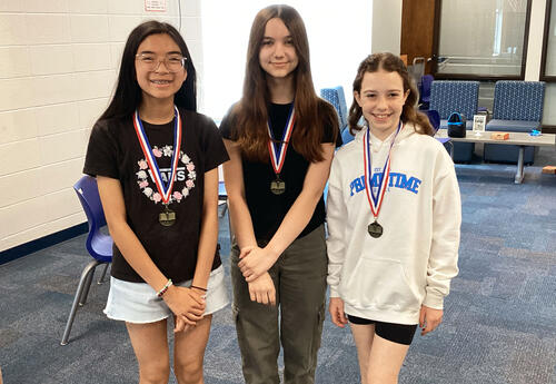 Three Middle School students pose with medals around their neck after winning Battle of the Books.