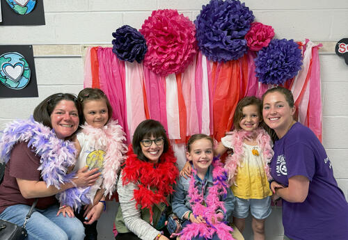 Moms and daughters pose with color boas and backdrop at Mom's Spa Night