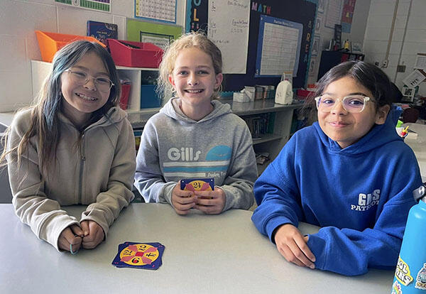 Three fifth grade girls smile while playing card game