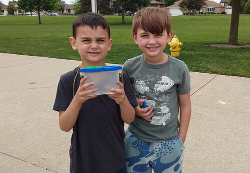 Students smile while holding container of insects outside