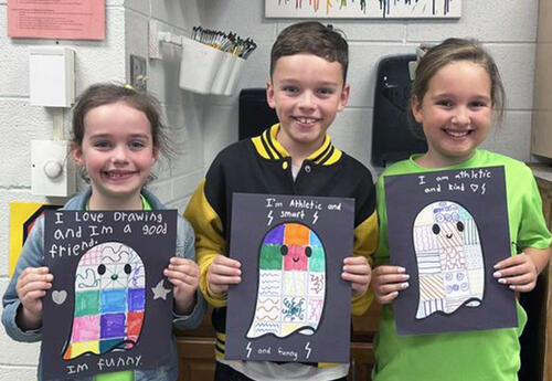 Students pose proudly with ghost quilt math pictures during Spooky Reading Night