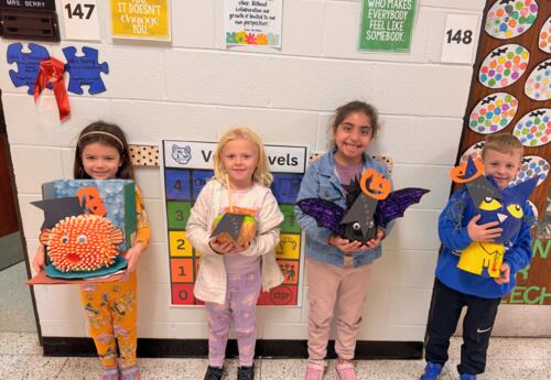 Students pose proudly with decorated pumpkins in school hallway