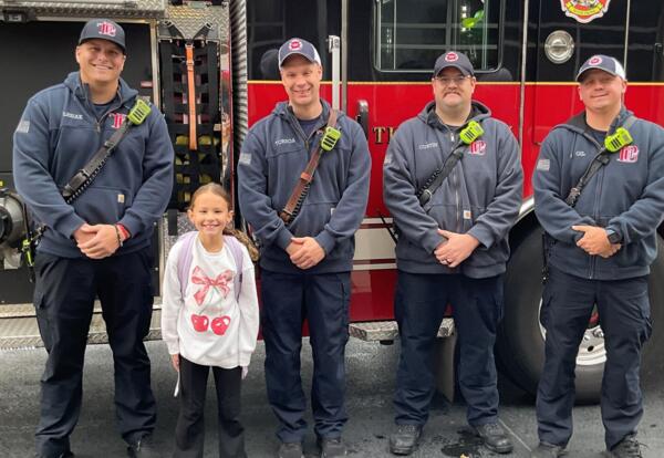 Fire prevention poster contest winner poses proudly with fire fighters in from of fire truck