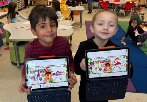 Two students pose proudly with iPads displaying gingerbread project