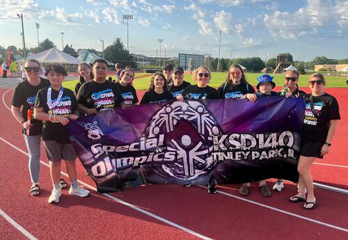 Student-athletes and coaches smiles while proudly holding up KSD 140 banner summer games
