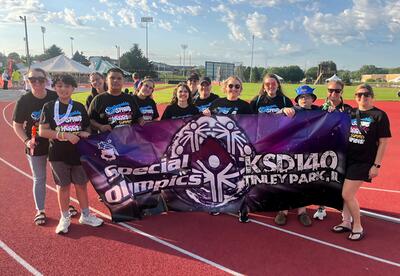 Student-athletes and coaches smiles while proudly holding up KSD 140 banner summer games