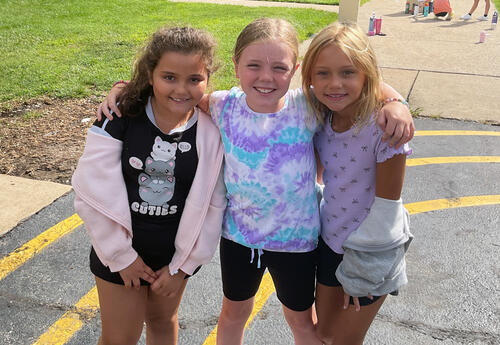 Three girls smiling with arms around each other outside.