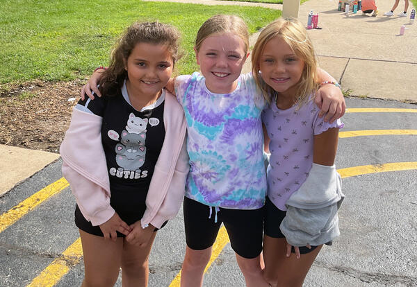 Three girls smiling with arms around each other outside.