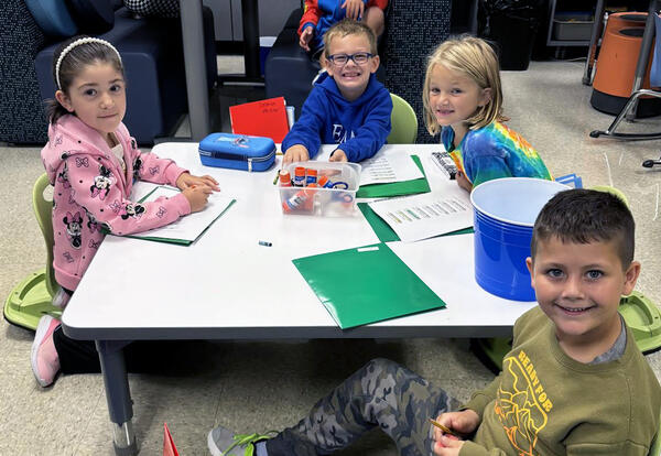 Four young students sitting at a classroom table and smiling.