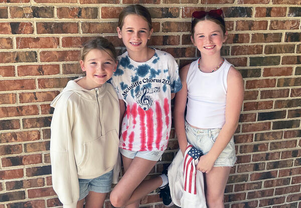 Three girls smile outside Christa McAuliffe School wearing red, white and blue