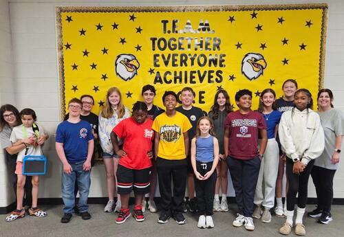 Prairie View September Students and Staff of the Month pose proudly in front of school bulletin board