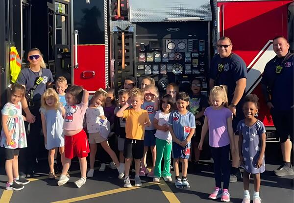 Firefighters pose with students in front of fire truck during their visit outside of Keller