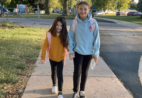 Two girls smile outside while walking to school