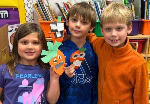 Three students smiling while holding up their crafts made at family reading night