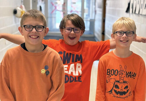 Three boys smile in the hallway while wearing orange shirts for Unity Day