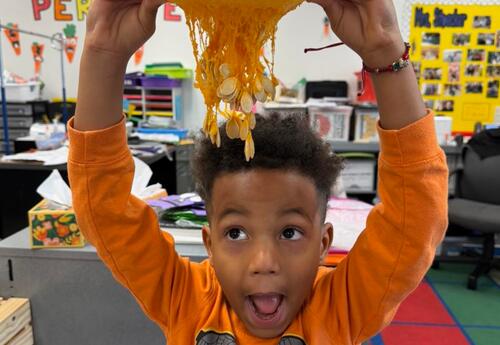 Student holding pumpkin over his head with pumpkin guts hanging out as he holds his mouth open