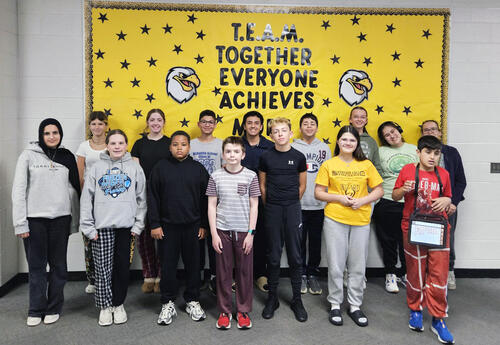 Prairie View October Students and Staff of the Month pose proudly in front of school bulletin board