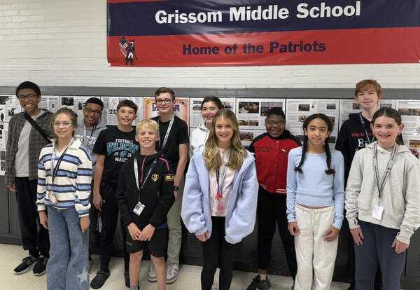 Twelve Grissom Students of the Month pose proudly in front of lockers and school banner