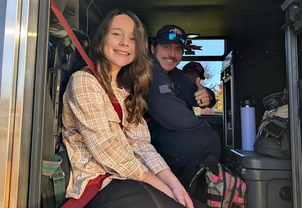 Fifth-grade fire prevention poster winner smiles in fire truck with fire fighter when she arrives at school