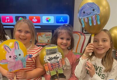 Three students smiling while holding handmade parade balloons