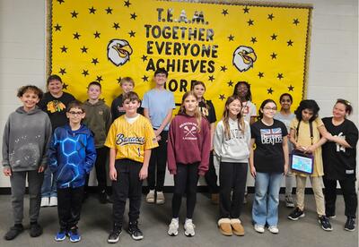 Prairie View November Students and Staff of the Month pose proudly in hallway in front on school bulletin board