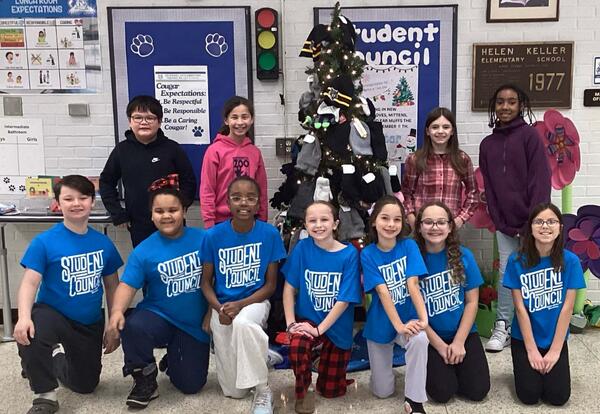 Keller students pose proudly in commons with donations from hat, glove, and mitten drive hanging on tree