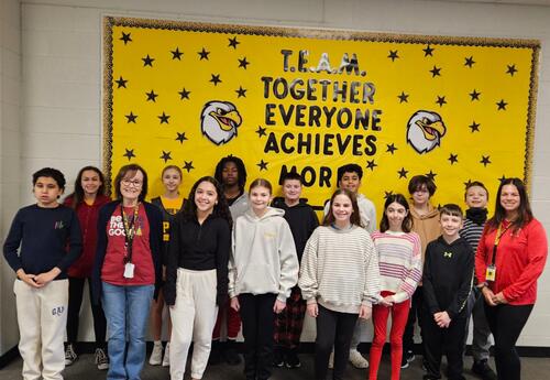 Prairie View December Students and Staff of the Month pose proudly in hallway in front on school bulletin board