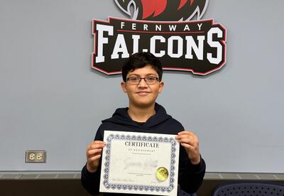 District Spelling Bee Winner poses proudly holding his certificate after winning in boardroom at Ad Center