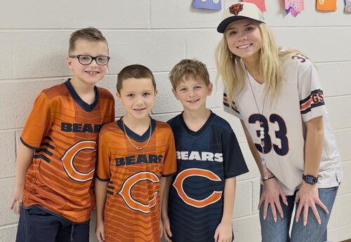 Three students smile and pose with teacher in school hallway on Chicago Bears Day