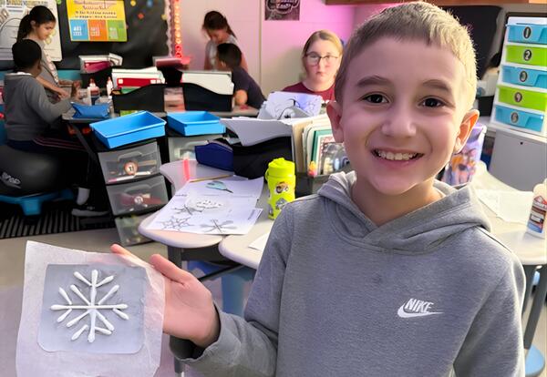 Student proudly holds up snowflake project in classroom