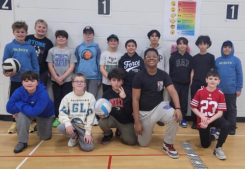 McAuliffe volleyball team stand and kneel in two rows in school gym after practice