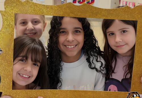 Four children smiling and posing together behind a large glittery gold frame.