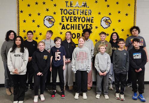 Prairie View January Students and Staff of the Month pose proudly in hallway in front on school bulletin board