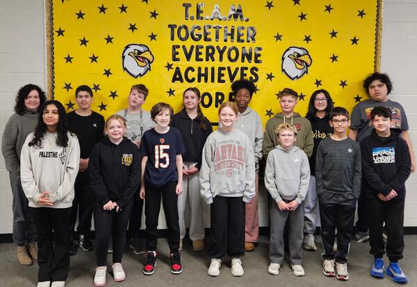 Prairie View January Students and Staff of the Month pose proudly in hallway in front on school bulletin board