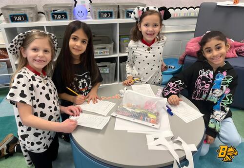 Four children wearing dalmatian-themed costumes and headbands are gathered around a round table, working on papers and crafts.