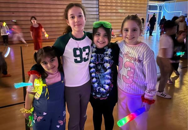 Four children pose for a photo at a glow-in-the-dark event. All children are holding glow sticks and appear to be smiling.